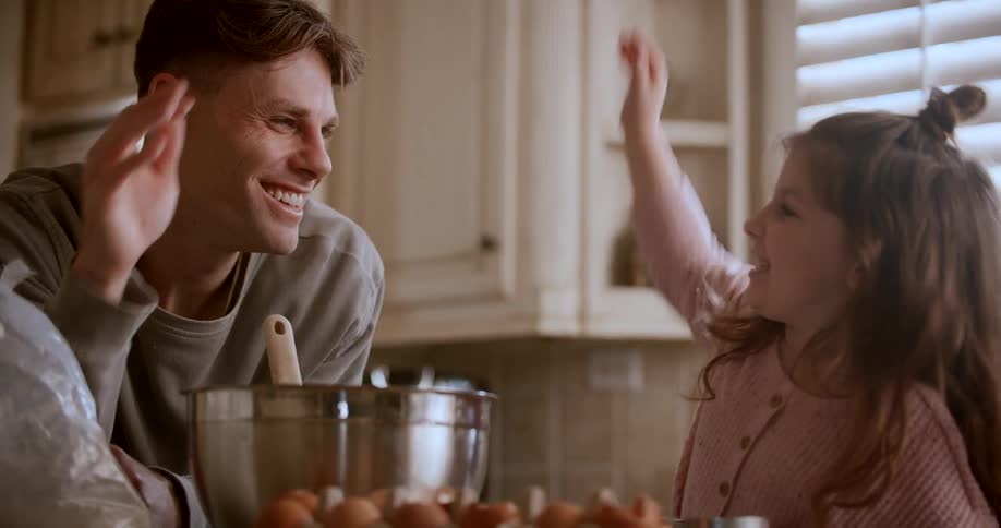 Father and daughter share a high five while cooking together at home