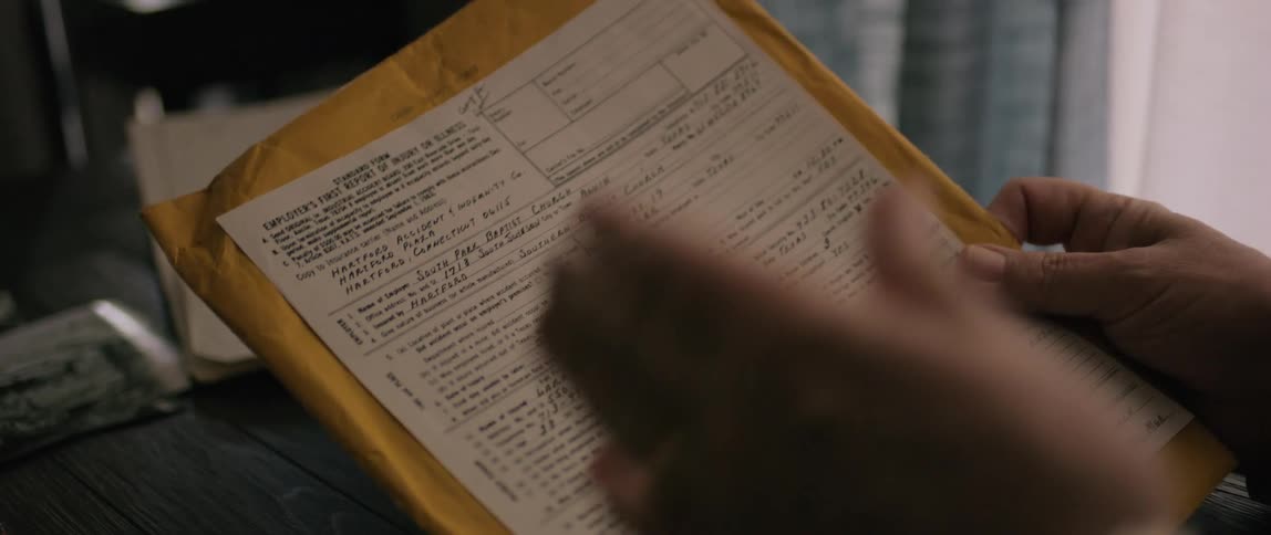 A man sitting at a desk is reading from a form while waving his left hand