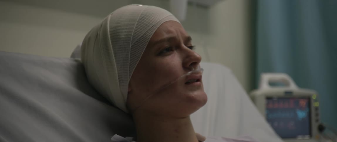 A woman with a bandage on her head bedridden in the hospital speaks slowly