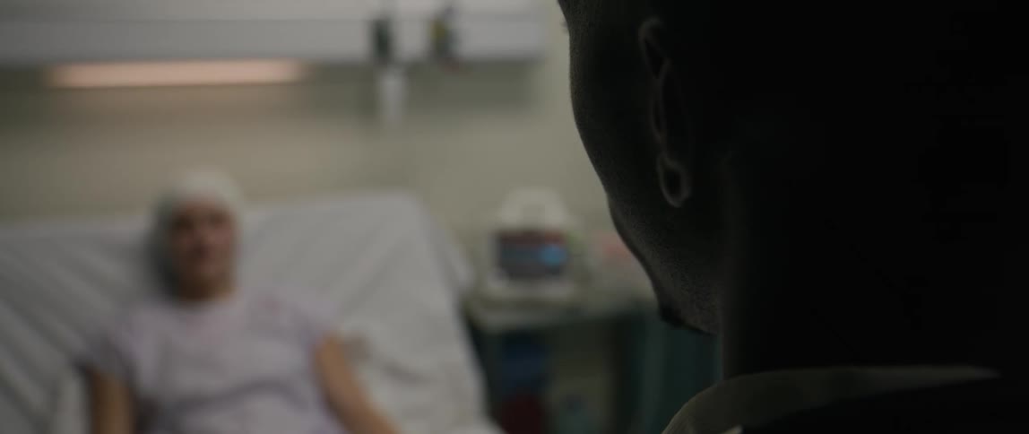 Man talking to a woman who is lying in a hospital room with equipment