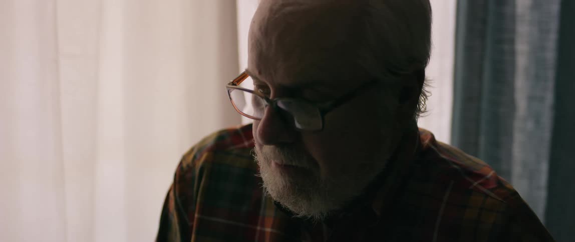 Elderly man is standing next to a window covered with curtains