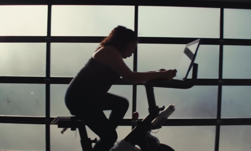 A silhouetted individual exercises on a stationary bicycle against a backdrop of multipaned windows