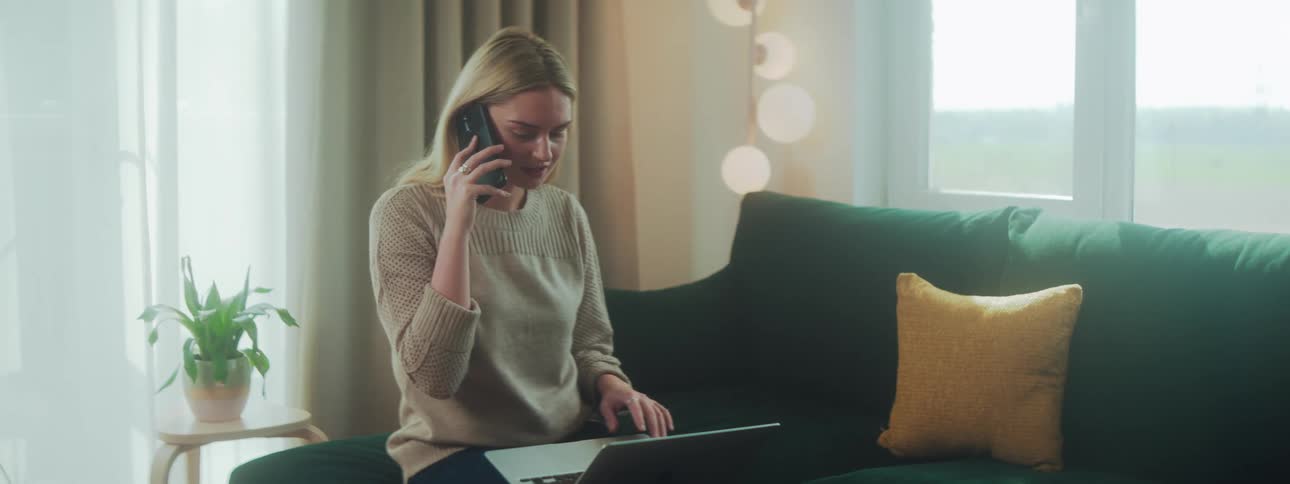 Woman on a phone call sitting and interacting with a laptop