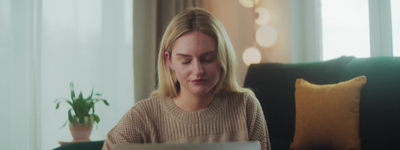 A woman is sitting on a green couch with her laptop