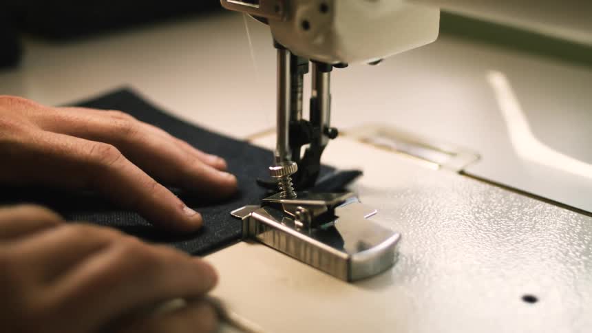 The tailor feeds fabric through the sewing machine