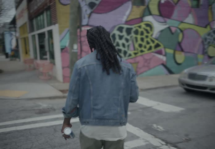 View of a man from behind with dreadlocks crossing the street through the urban city