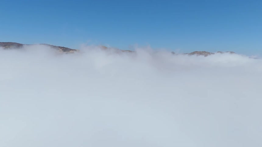 Aerial view of a sea of clouds revealing mountains in the background
