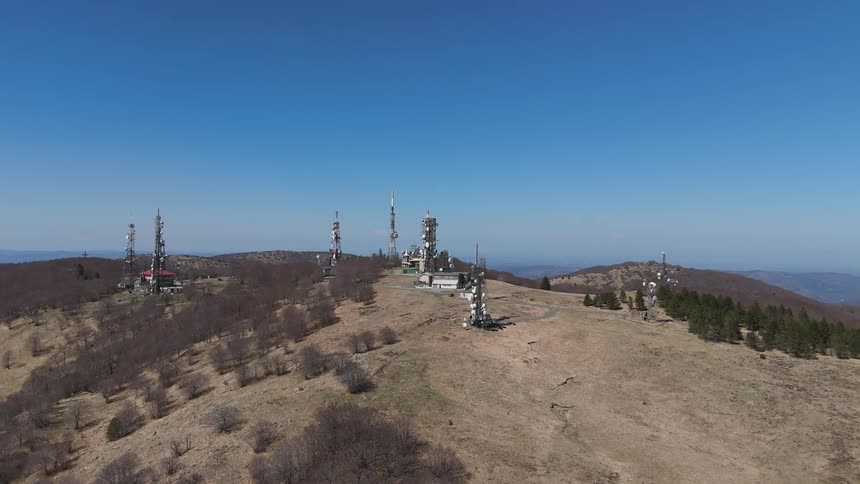 Several towers spaced away from each other sitting on top of a mountain with trees and weeds dotting it