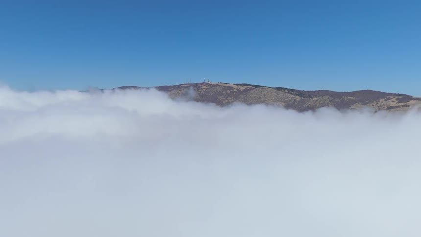 Louds and mountains under a blue sky with buildings on the horizon