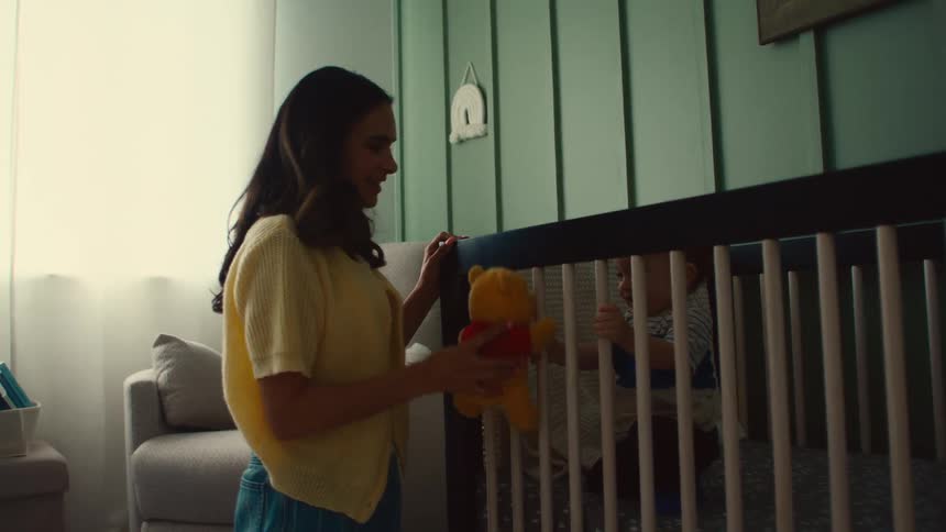 Woman playfully holds a stuffed toy in front of a baby in a crib