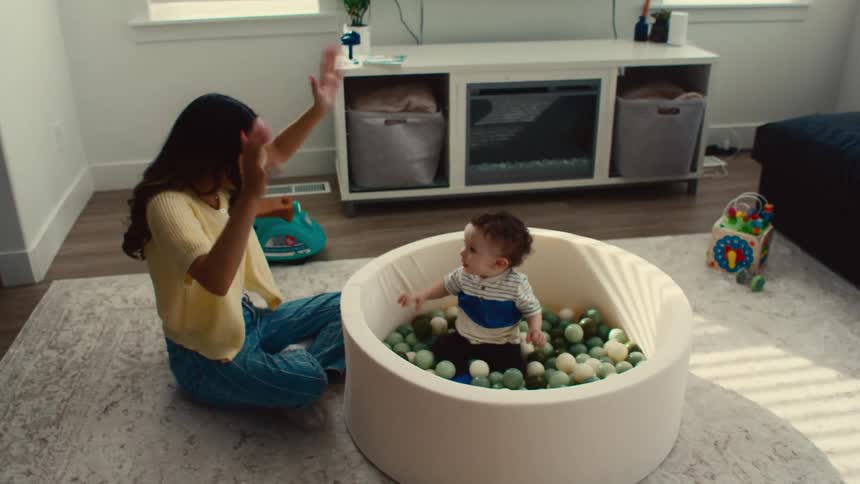 Mom tossing balls to baby sitting in ball pit then dancing while sitting on floor