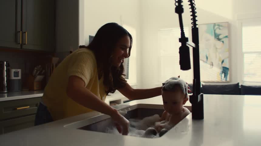 Mother bathing her daughter in the kitchen sink