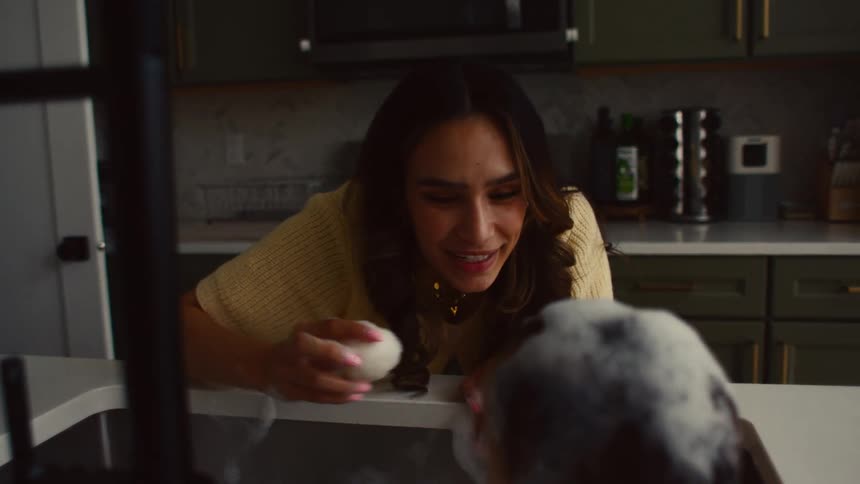 Mother is playing with her infant son while giving him a bath in the kitchen island sink