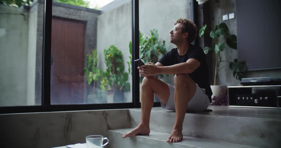 A sad man is sitting on a marble step while texting on his smart phone
