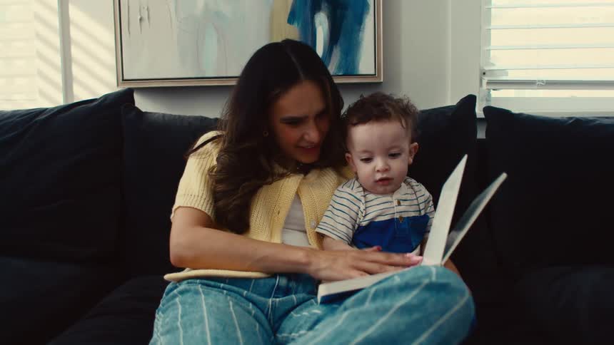 Mother sitting on the couch with her little son and reading a book