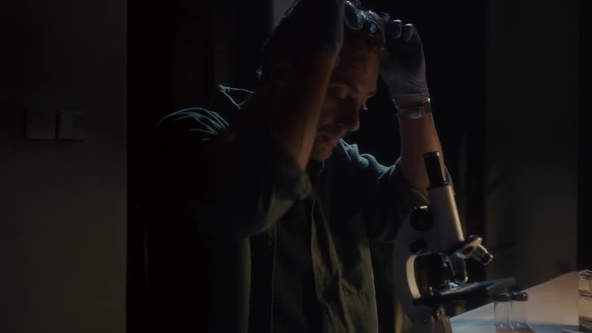 Man using a magnifying glass with medical equipment on a lowlit table