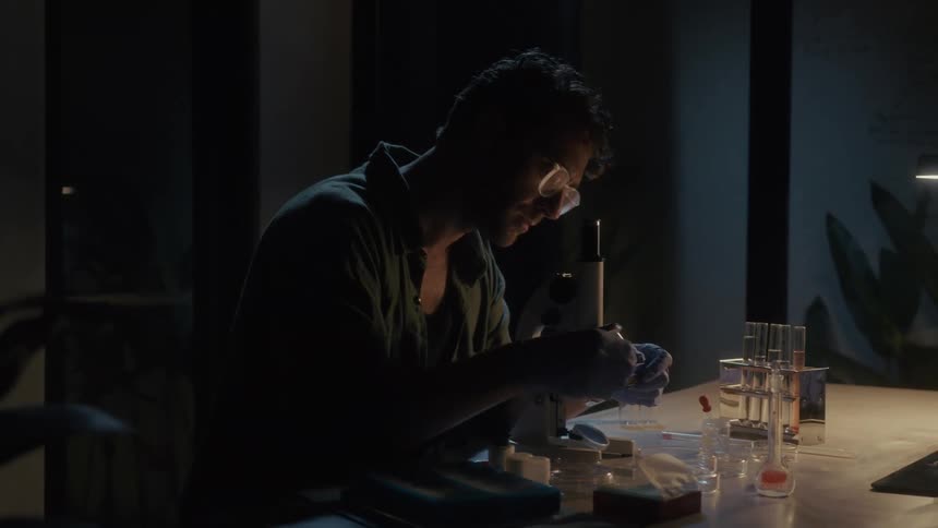A man is placing samples under the microscope while doing research at home