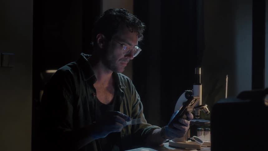 Man in glasses examining a laboratory sample and holding a smartphone