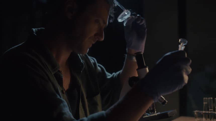 A man wears his glasses as he carefully inspects the contents of a bottle