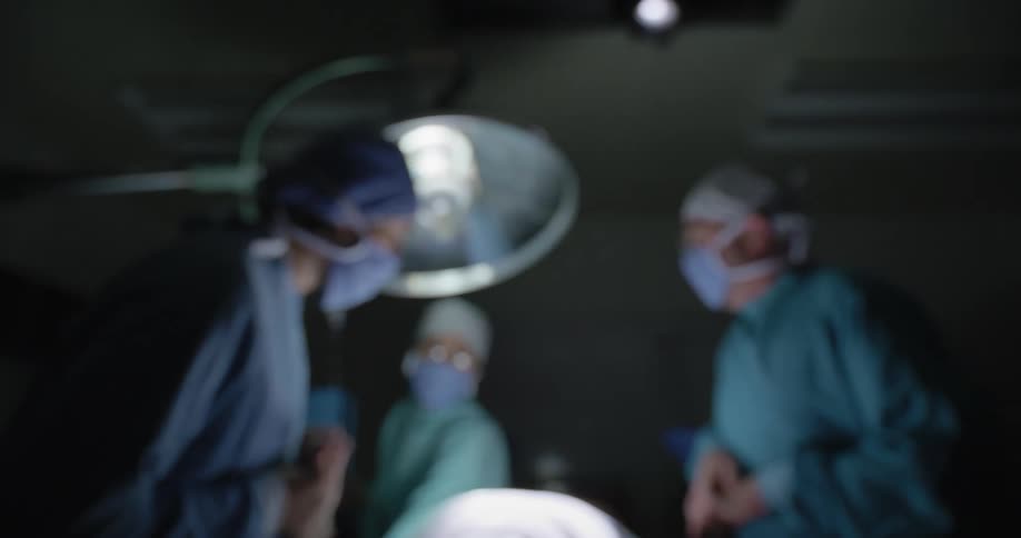 One medical professional gives chest compressions to a patient while two other medical professionals stand nearby