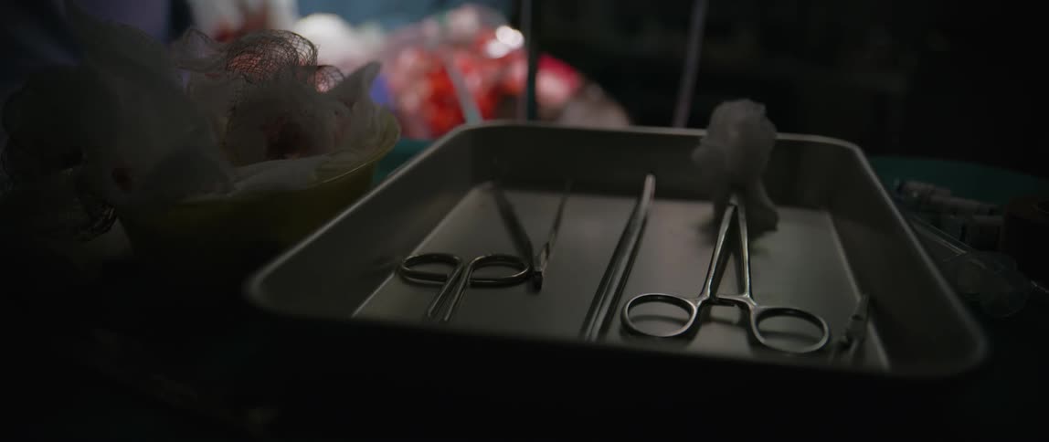 A person picks up a pair of forceps from a sterile tray while wearing gloves