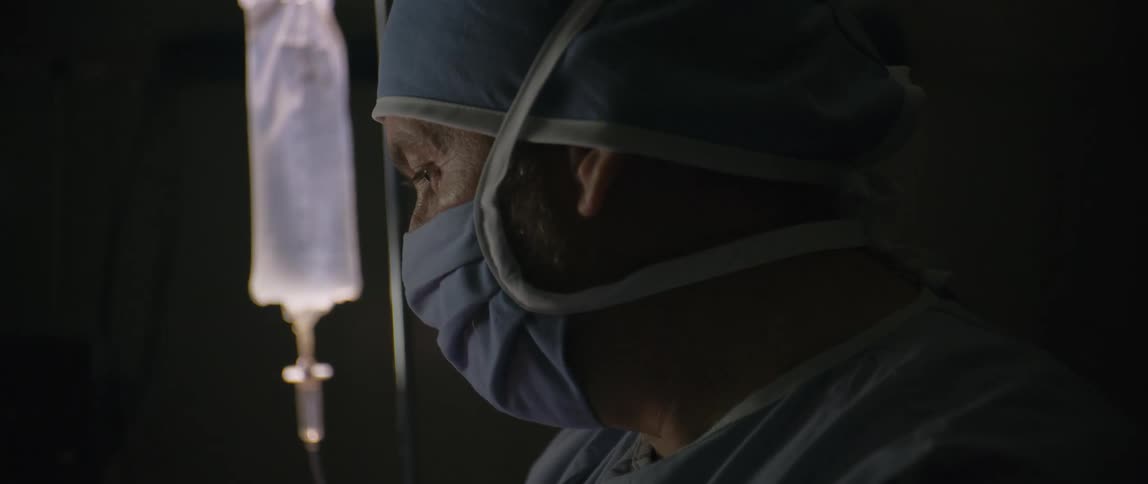 Doctor wearing scrubs and face mask near an iv bar talking and nodding his head