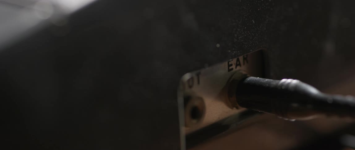 A hand plugs an audio cable into a socket labeled ear on a closeup electronic device