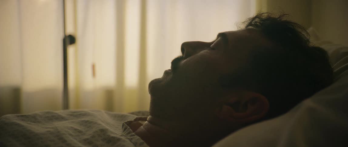 A man lies asleep in a room with sheer curtains