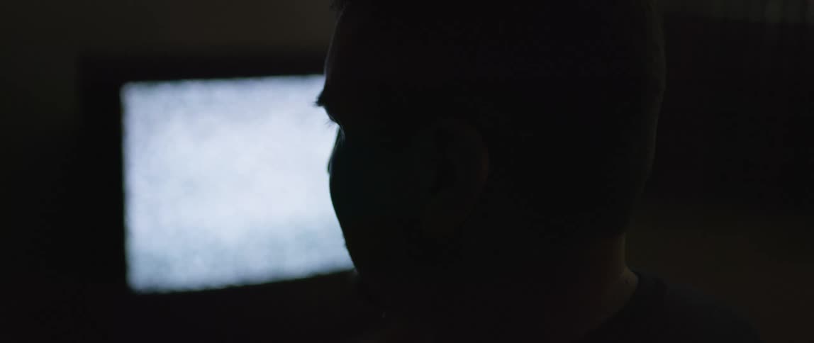 A man is in a dark room with a static filled television running