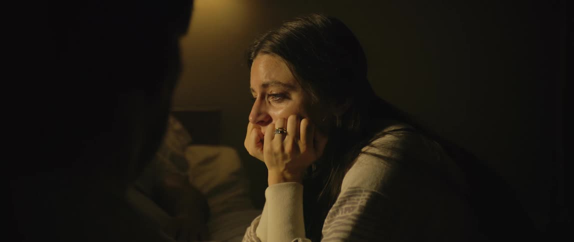 A woman has her face in her hands crying while she visits a man in the hospital