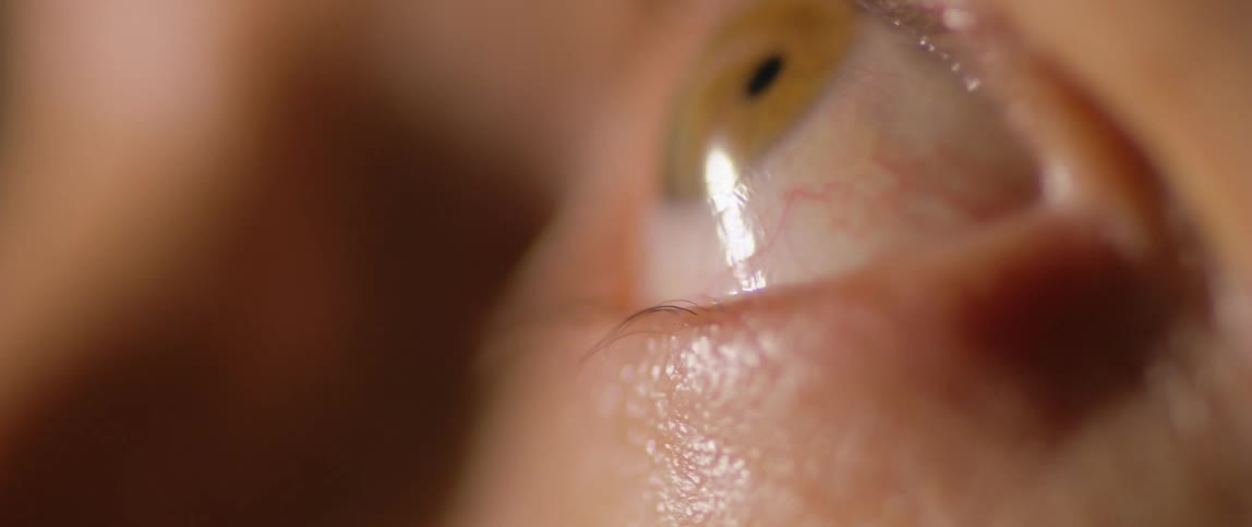 A persons eye with a green iris that is blinking and looking sideways