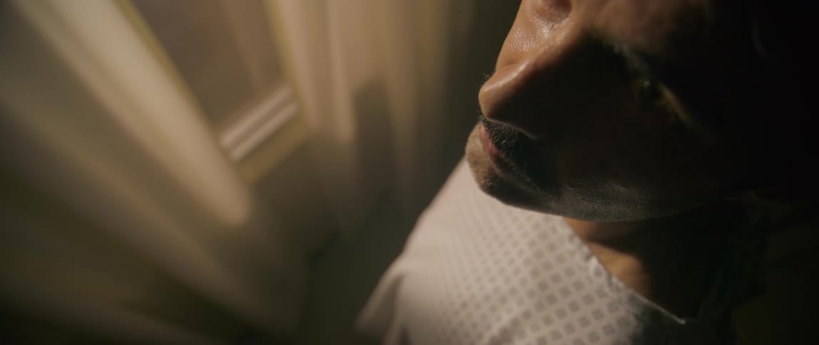 A man in a hospital room standing in front of the window staring upward and blinking repeatedly