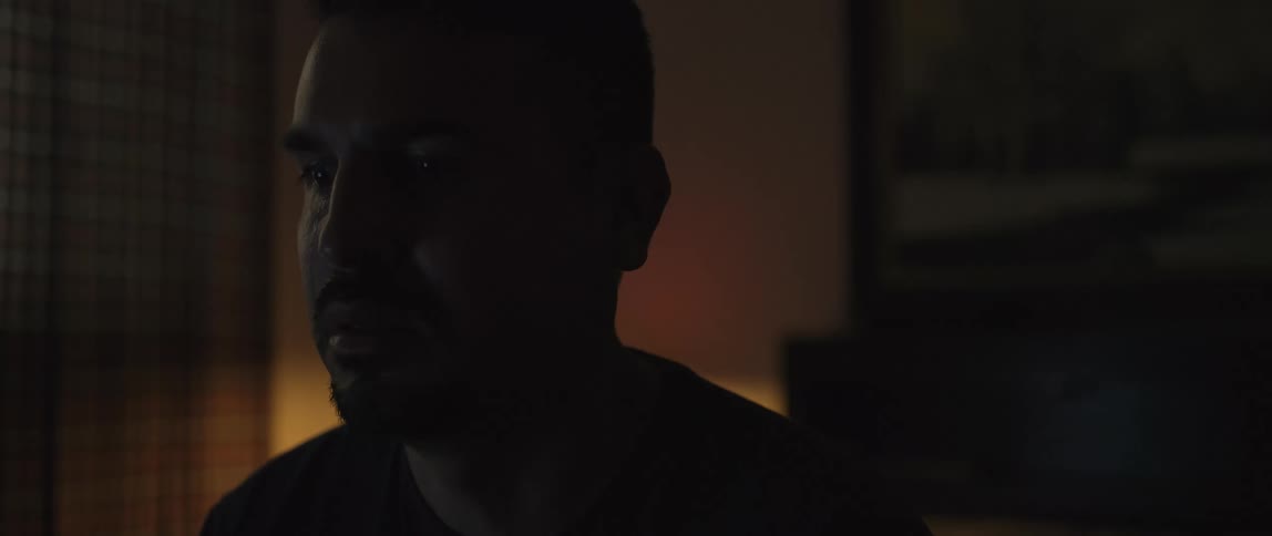 A male with a mustache and goatee from the shoulders up staring in a dark room