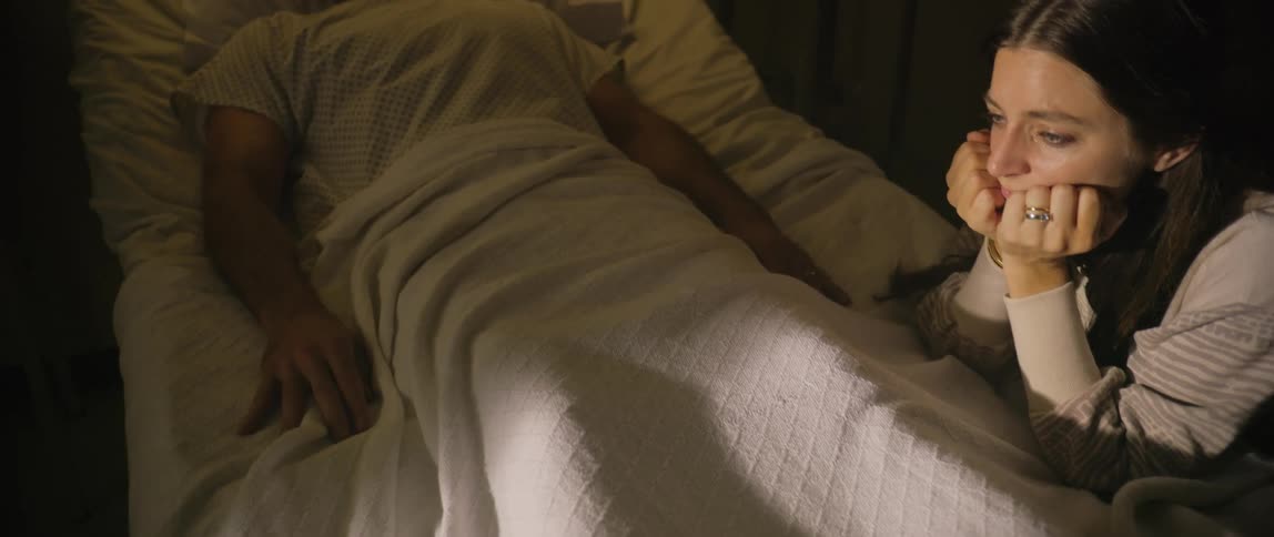Woman leans on the hospital bed while visiting a male patient