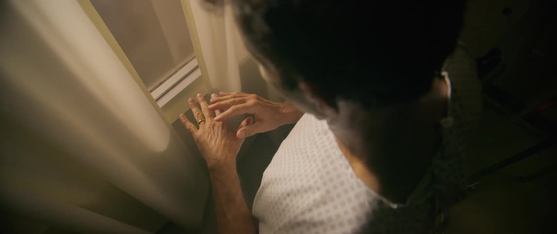 A hospital patient looks at his hands by the window