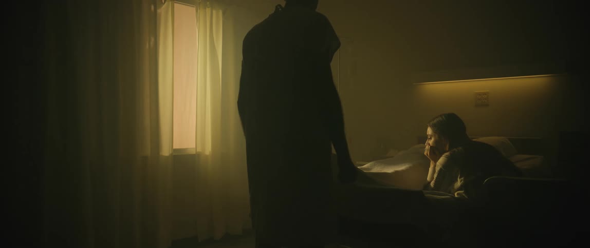 Hospital patient moving outside his body crouches down next to the woman waiting by his bedside