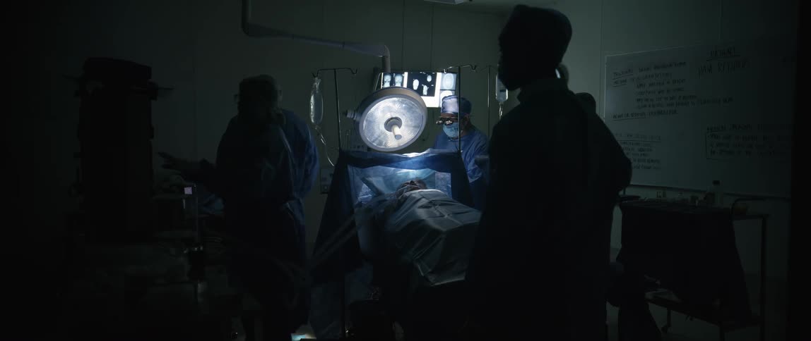 A groups of draped surgeons surround a patient while performing a surgery
