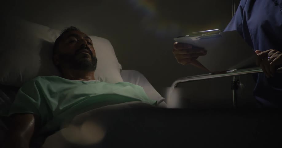 Medical professional consults a patient chart while attending a sleeping hospital patient