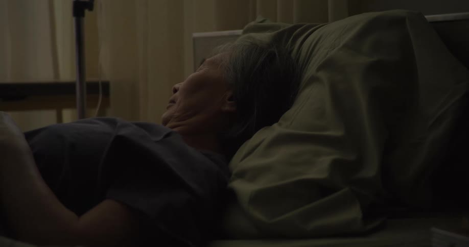 A person lies in bed seemingly unwell and surrounded by a somber atmosphere suggesting vulnerability and perhaps illness