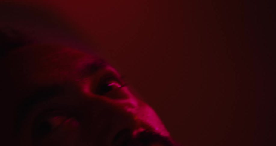 Man under a red light sweating and looking up with wide eyes shaking his head