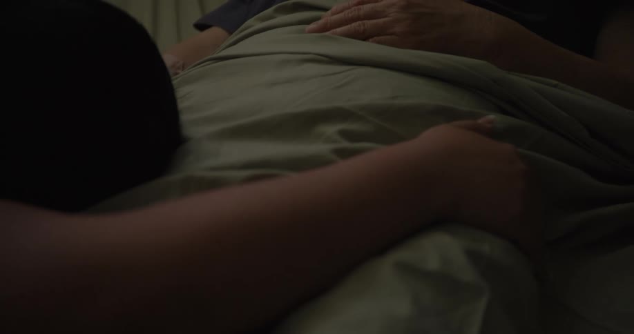 A visitor is crying and holding a patients hand