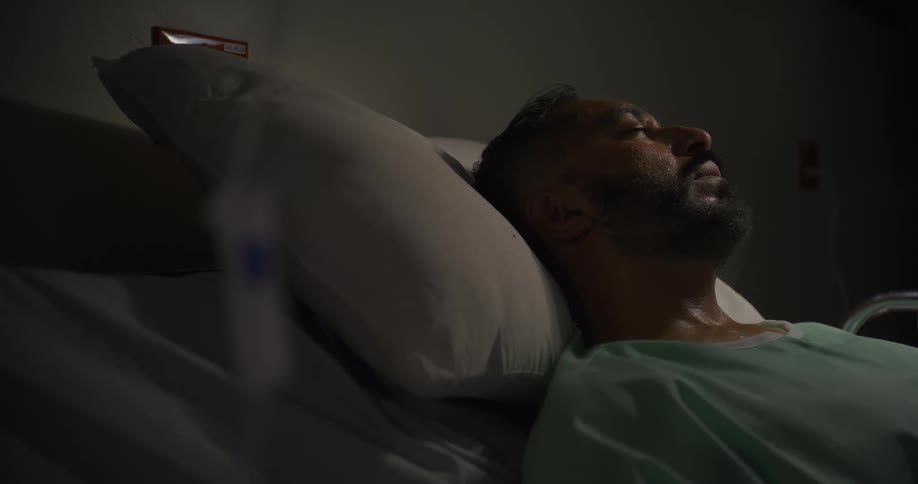 Man nods and shakes his head as he takes deep breaths while lying down on a hospital bed