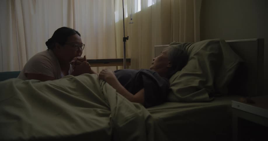 A crying woman holds the hand of a elderly hospital patient