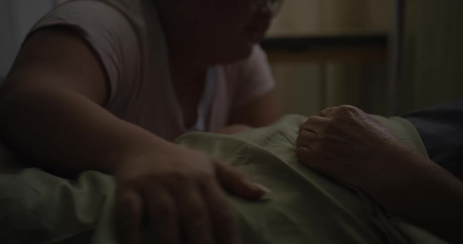 Woman cries while comforting an invalid lying in bed