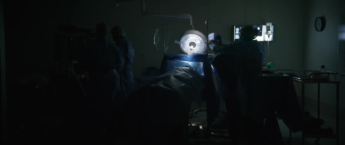 A group of draped surgeons move around in an operating theater preparing for a surgery