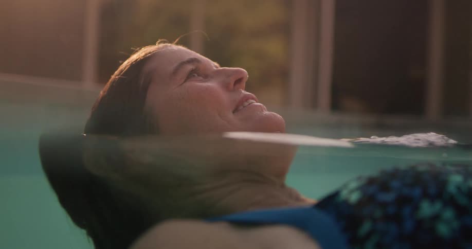 A woman relaxes in a pool bathed in warm sunlight and framed by a modern architectural setting