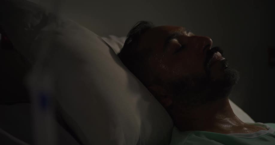 A man nods and turns his head from side to side as he takes deep breaths while lying down