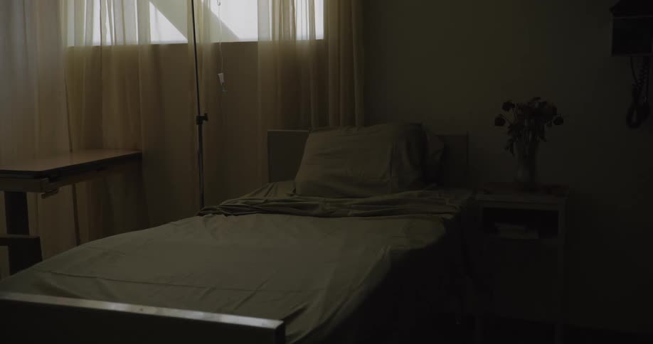 A bed nightstand and iv pole with an iv bag are set up in a hospital room