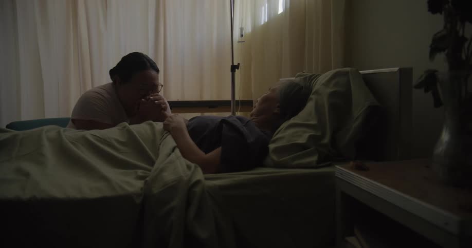 Daughter holding hands with her mother hospitalized in a room