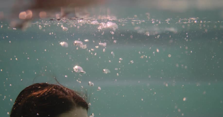 The face of a woman who is underwater releasing many bubbles and going to the surface and her eyes are open